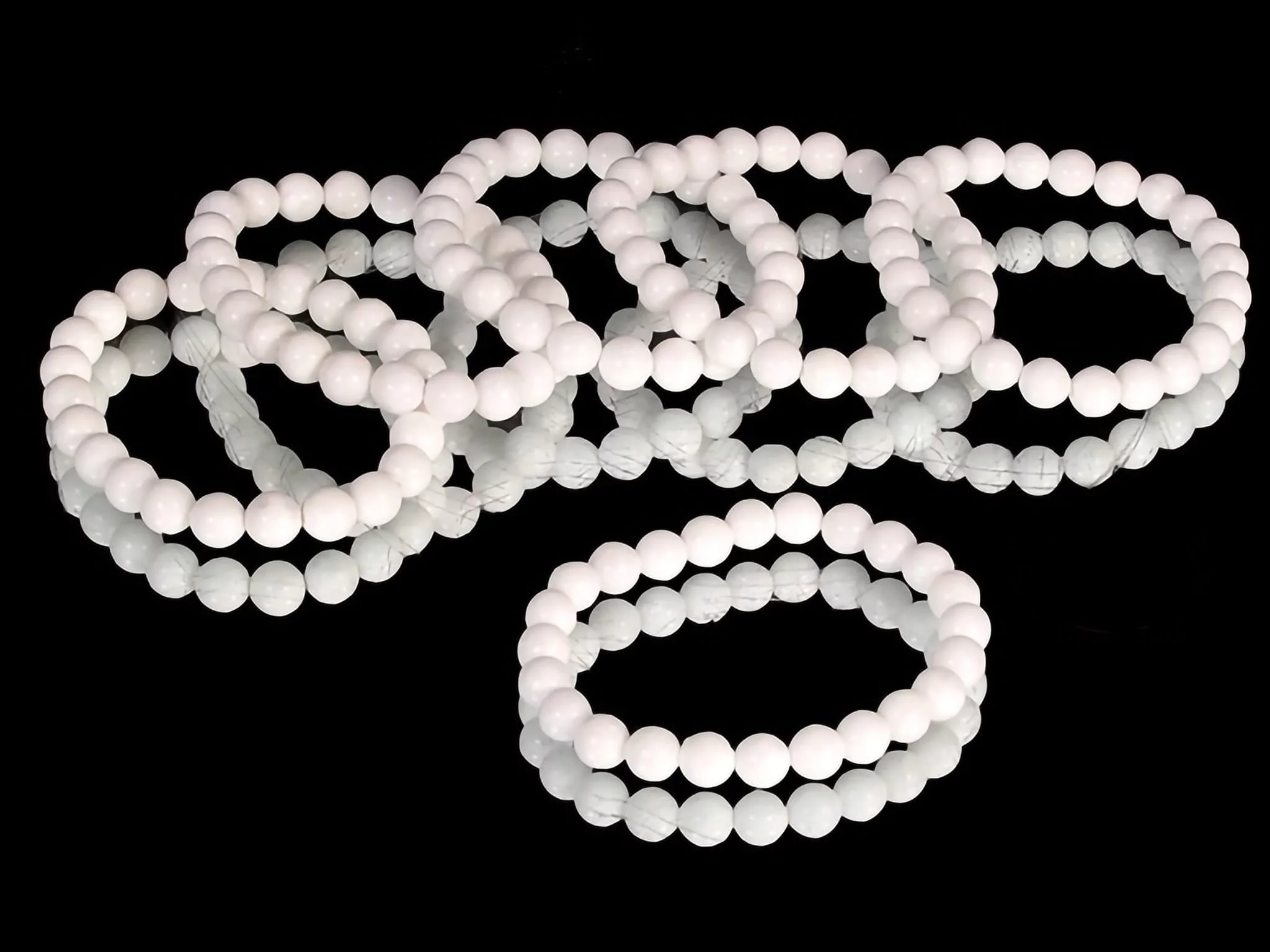 Barite gemstone bracelet with white round beads, arranged multiple times on black background