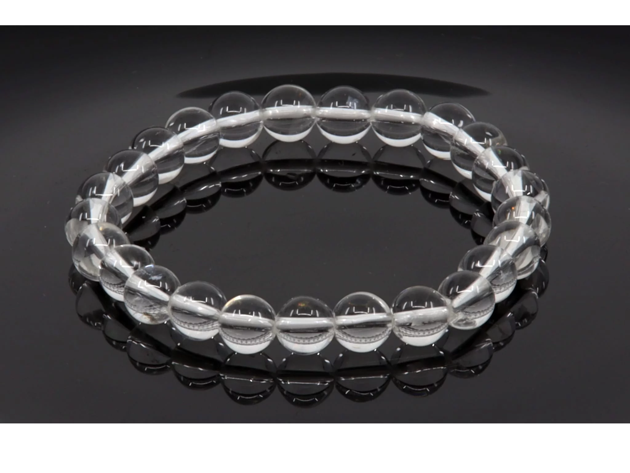 Bracelet en pierres précieuses en cristal de roche avec perles transparentes sur surface noire miroir