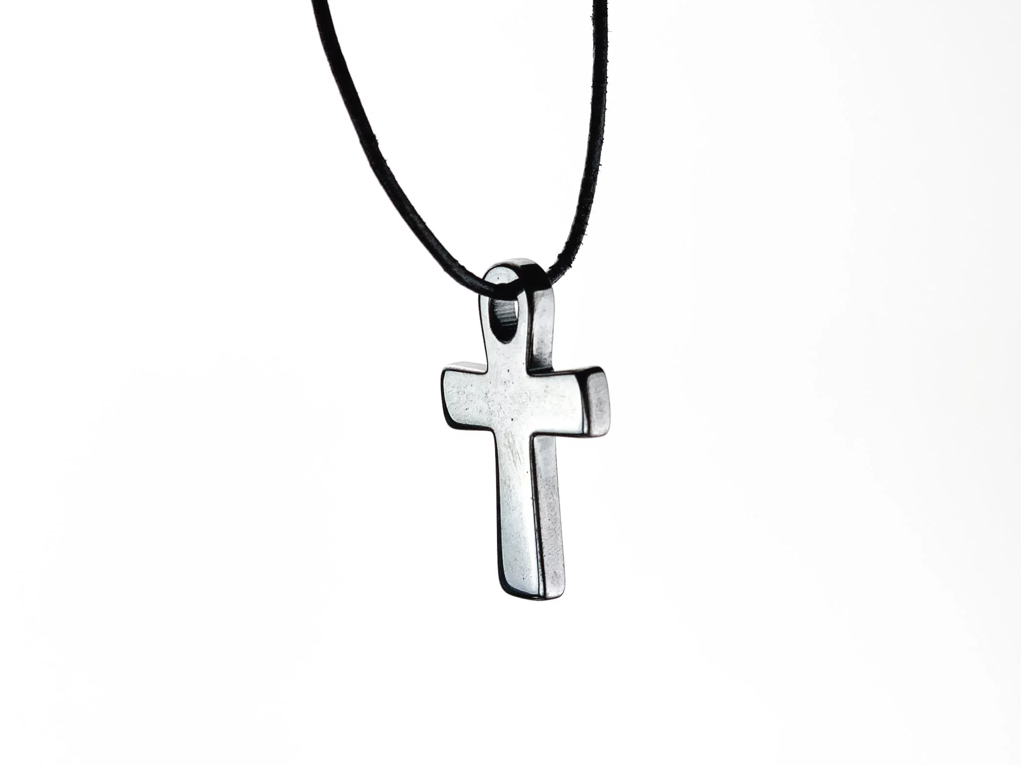 Pendentif croix en hématine suspendu à un collier noir sur fond blanc