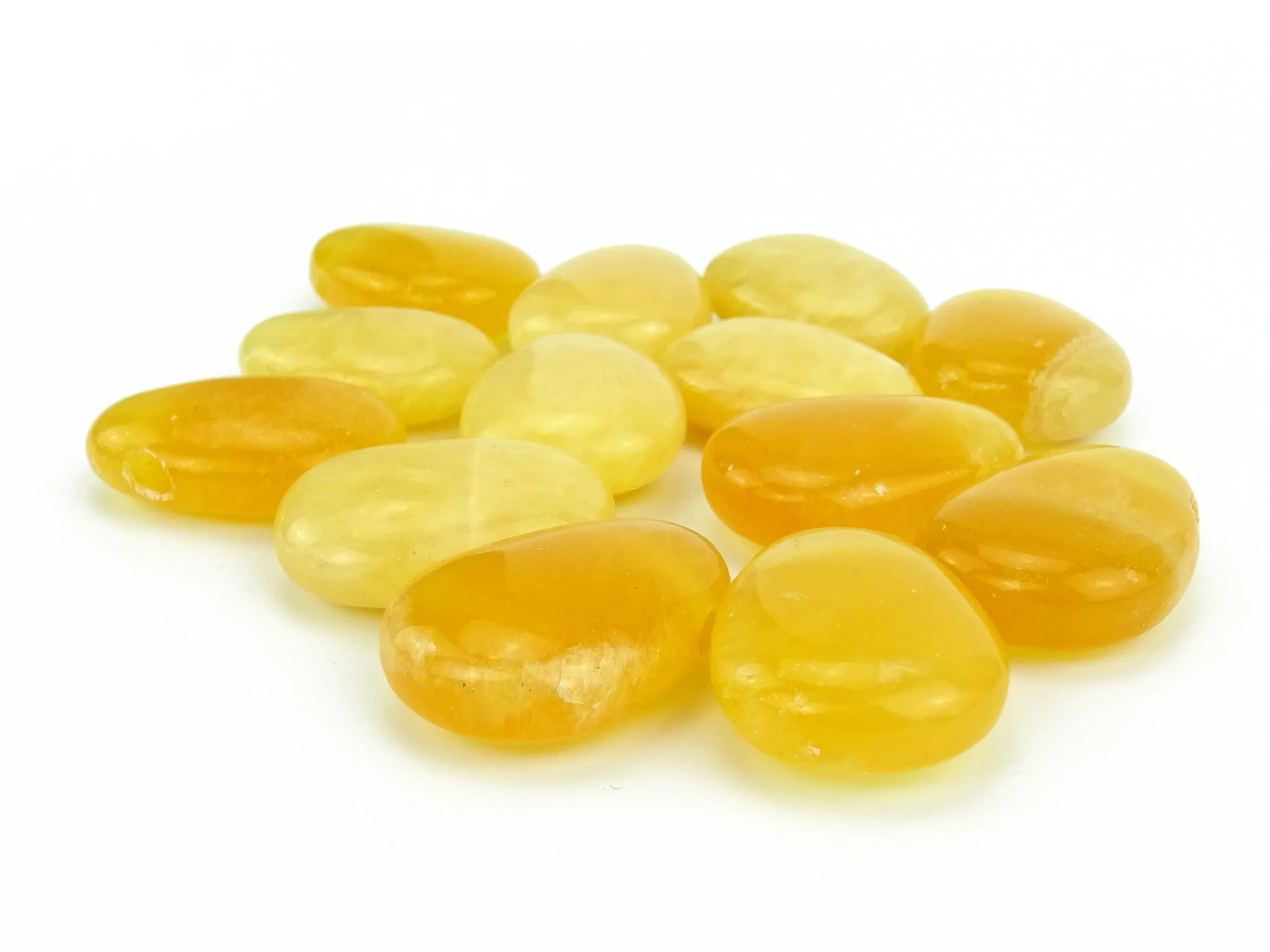 Orange calcite gemstone as a selection of smoothly polished yellow-orange tumbled stones on a white background