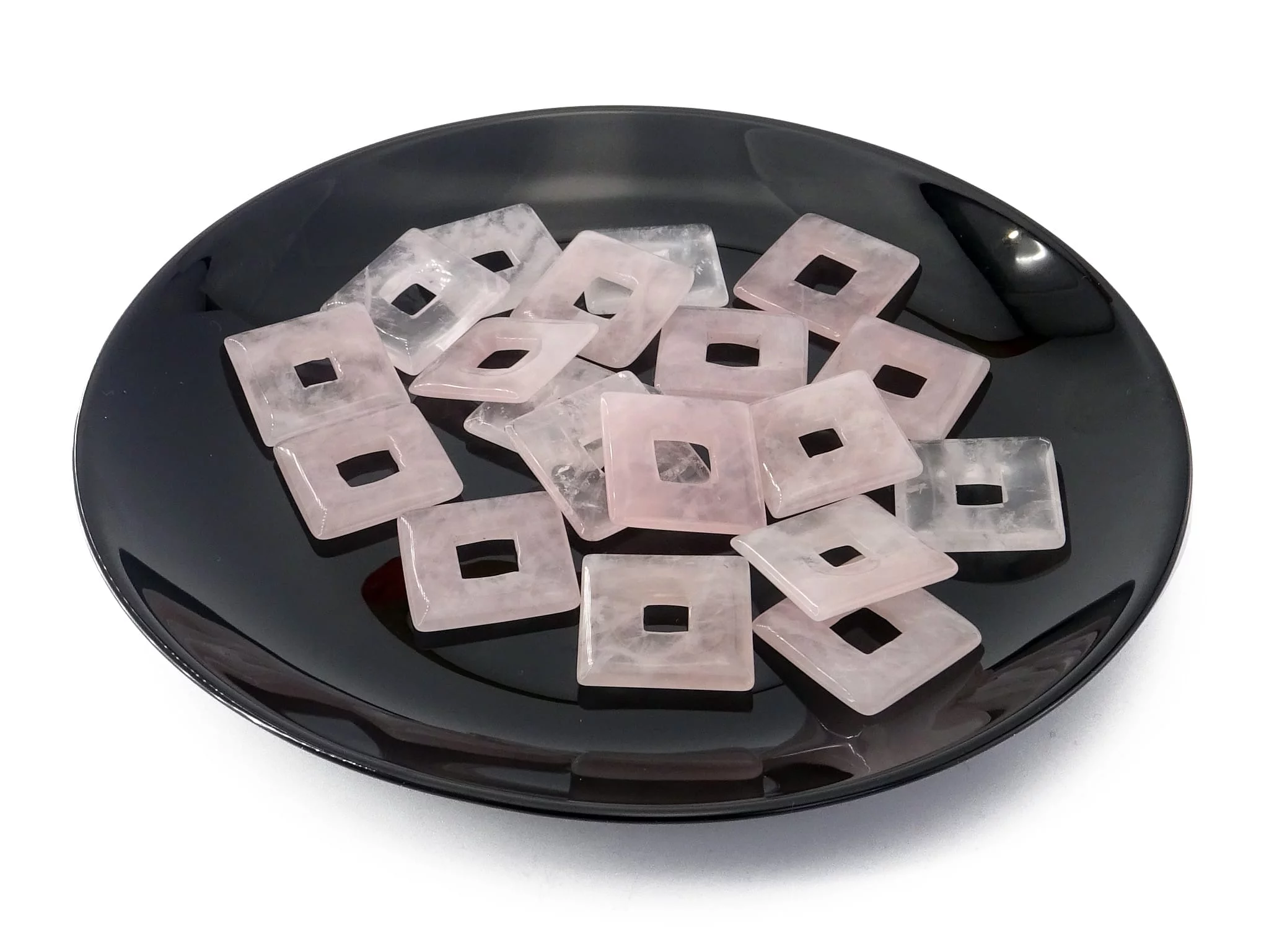 Rose quartz square donut pendant as multiple polished holed stones on black dish