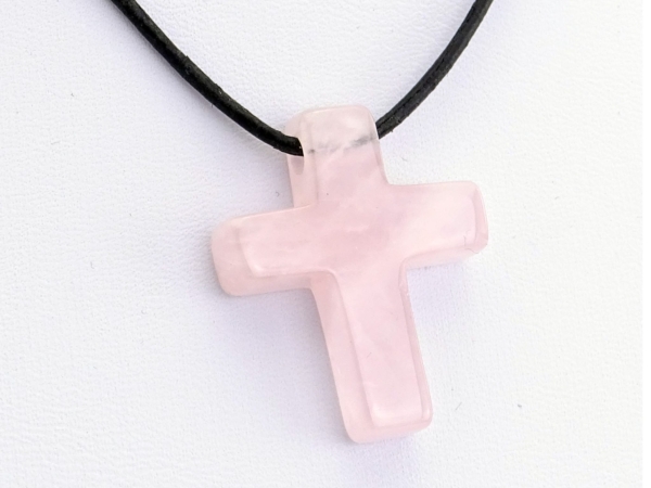 Pendentif croix en quartz rose en gros plan avec collier en cuir noir et surface polie
