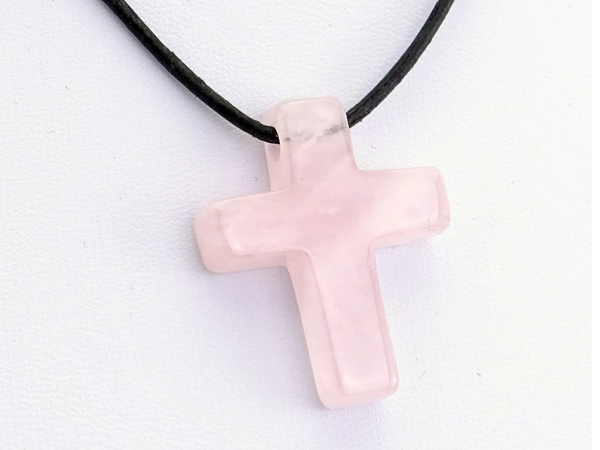 Pendentif croix en quartz rose en gros plan avec collier en cuir noir et surface polie