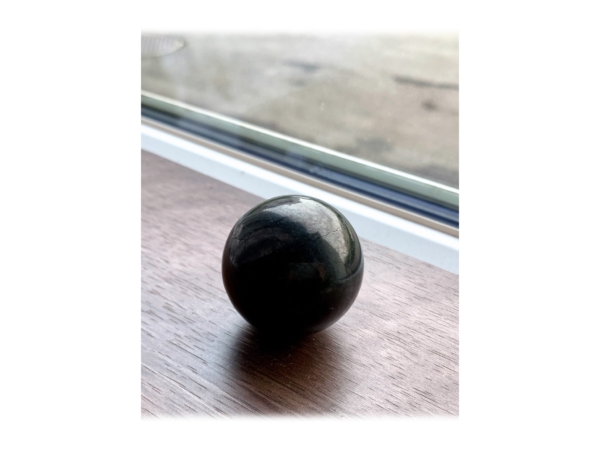 Polished shungite sphere on a wooden surface in front of a window in side perspective
