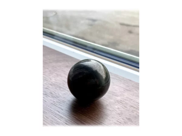 Schungit Kugel glänzend auf einer Holzfläche vor einem Fenster in seitlicher Perspektive