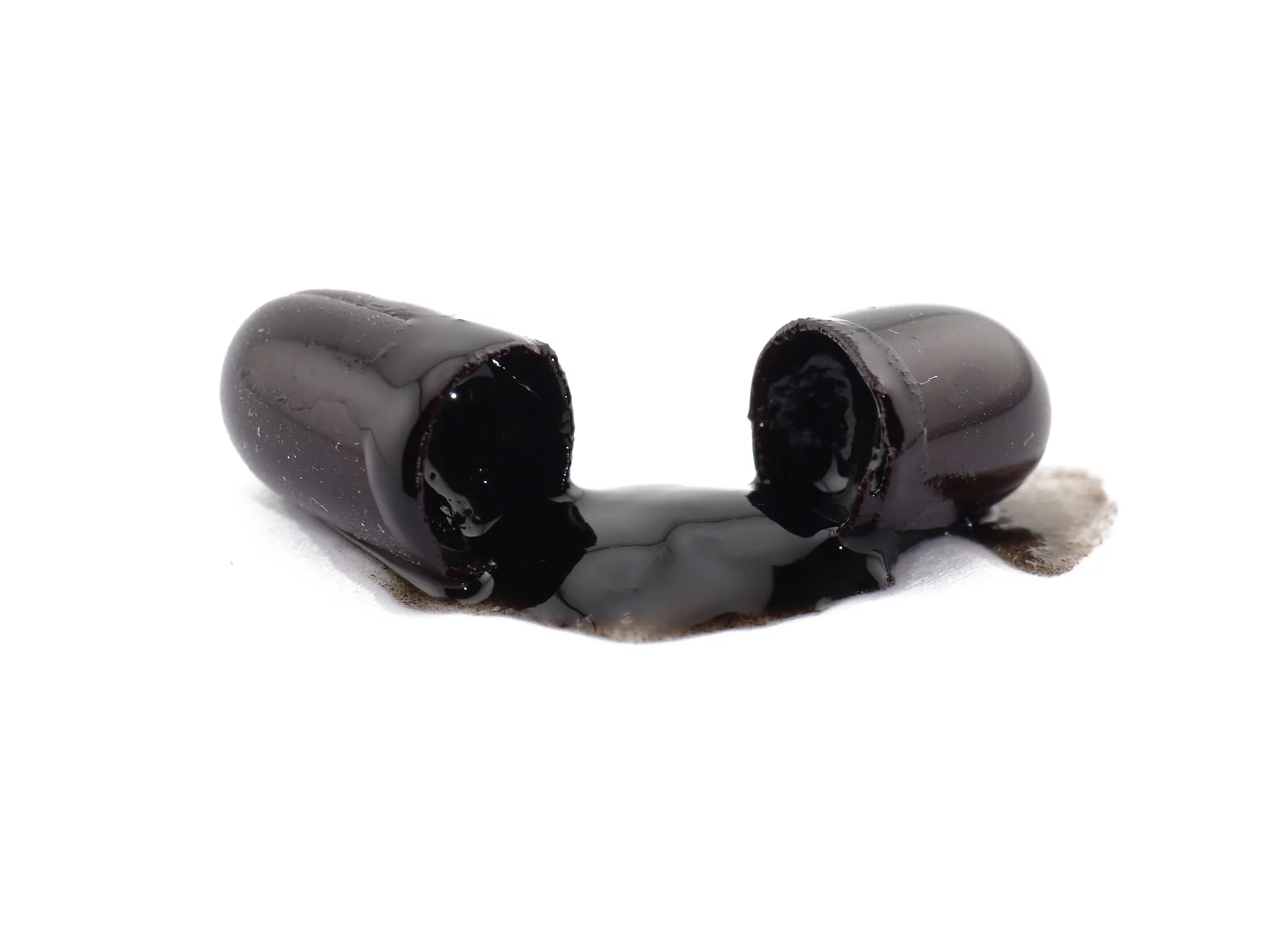 Shilajit softgel capsules opened with visible dark content on a white background