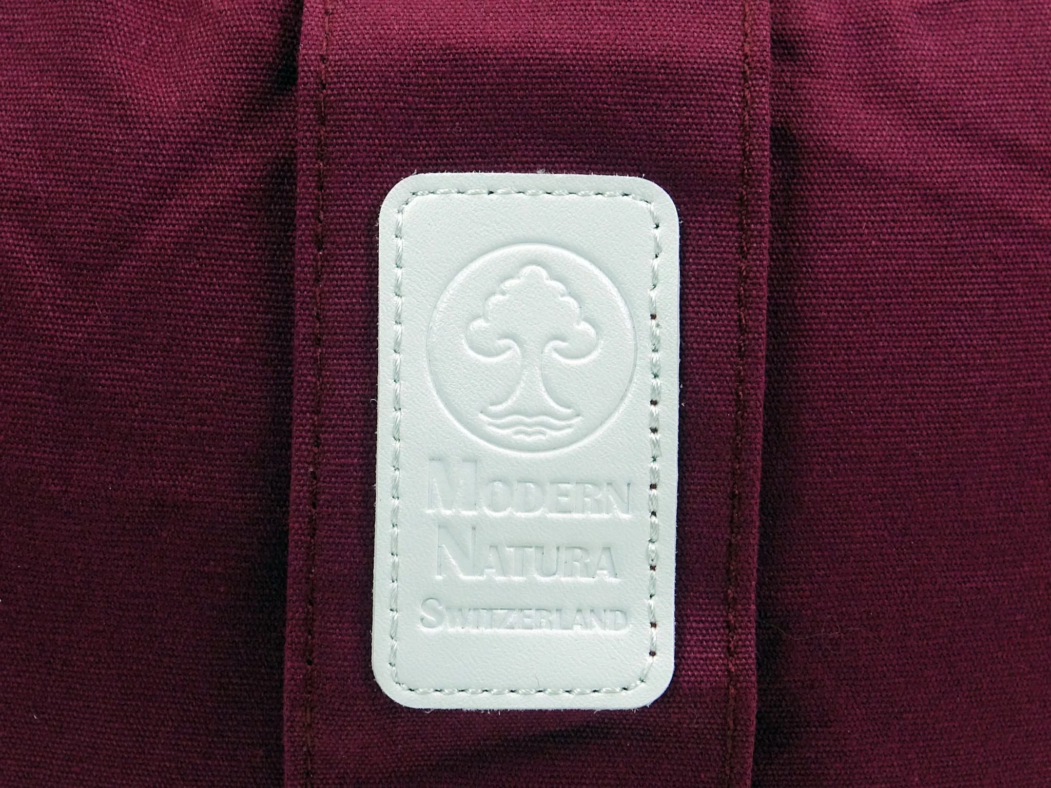 Yogakissen Vino mit Detailansicht des weissen Modern Natura Markenlabels auf weinrotem Stoff